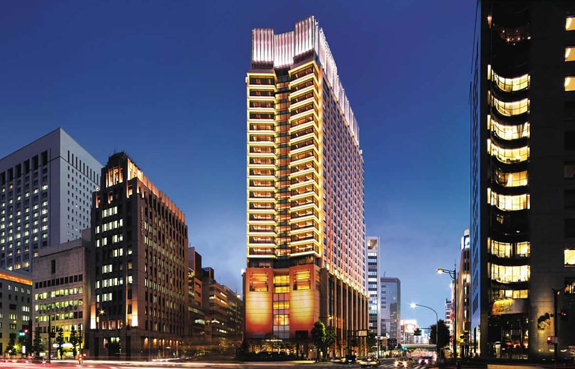 The Peninsula Hotel in Tokyo Japan lit up at night next to other hotels above a busy street