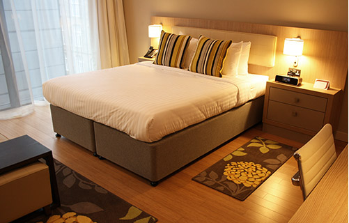 A hotel room with a wooden floor and a cream double bed, dimly lit by two lamps on bedside tables
